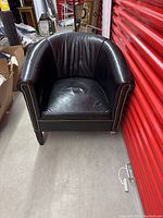 Front view of black leather bucket armchair showing studded detailing on arms and condition of leather seat and backrest.