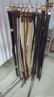 Front view of men's belts hanging on a rack showing variety of colors and buckle types