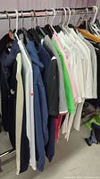 Side view of clothing rack showing multiple men's sportswear tops including jackets and polo shirts in different colors and brands, all size medium.