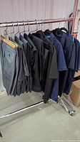 Long view of black and blue men's sports shirts and two pairs of grey shorts hanging on metal clothing rack.
