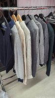 Side view of the sweaters on hangers showing various textures and colors including solid, striped, and button-up collar sweaters.