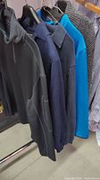 Five men's sweaters and one dress shirt on hangers showing color and fabric textures.