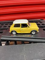 Yellow and white 1960 Mini Cooper miniature model side view with closed doors on display base.