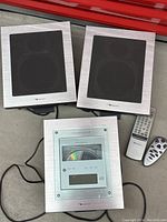 Two silver-finish speakers, central disc player and two remotes arranged on floor