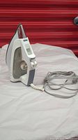 Side angle view of the white and gray Rowenta Focus High Precision steam iron with power cord extended on surface