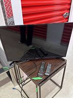 Samsung 32-inch TV on stand with four remote controls and cables visible.