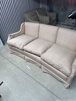 Beige fabric three-seater couch with removable cushions, curved backrest, and skirted bottom shown from a side angle.
