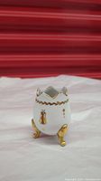 Photo of the Limoges egg-shaped vase showing one side with gold painted emblem, gold rim, and gold legs.