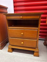 Front view of the wooden side table showing two drawers and an open cubby space with round wooden knobs on drawers.