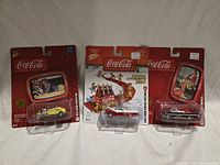 Three sealed Coca-Cola diecast cars in blister packs