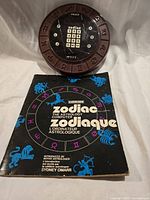 Front view of Coleco Zodiac computer alongside booklet