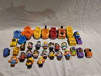 Overview of all Little People figures and Wheelies vehicles laid out on cloth backdrop