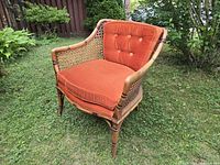 Front angled view of bamboo and cane armchair with orange cushions