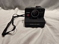 Front view showing lens, red shutter button, Polaroid Land Camera logo, wrist strap