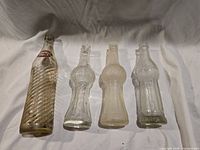 Four clear glass soda bottles laid side by side on white cloth