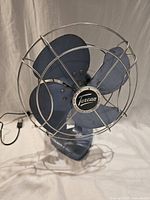 Front view of blue metal Torcan desk fan with chrome guard and badge