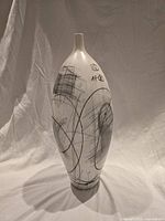 Full front view of tall white ceramic vase with abstract pencil drawings