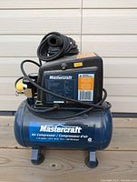 Side view of the Mastercraft air compressor showing overall condition, tank and motor with label and power cord coiled on top