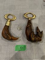 Two bottle openers side by side with a quarter for scale, one shaped like an eagle head and the other like a hunting dog holding a bird.