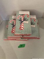 Eight unopened packages of Sweetzer & Orange Christmas cards stacked, showing holiday candy cane designs on the card fronts.