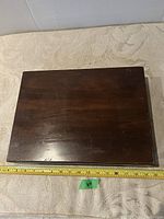 Closed wooden box with dark finish on a fabric surface and a measuring tape indicating dimensions around 14 inches wide.