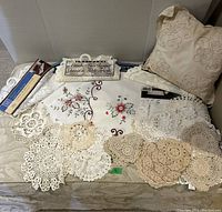 Crochet lace doilies and embroidered pillow arranged on fabric surface, showcasing variety of sizes and patterns.