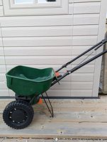 Side view of green fertilizer spreader showing large wheels, handle and hopper