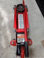 Top view of the red Motomaster hydraulic floor jack showing the lifting pad, handle, and warning label.