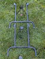 Two black metal folding table legs laid out on grass, showing folding hinges and mounting brackets.
