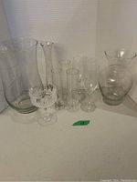 Nine assorted clear glass vases arranged on a white surface against a white backdrop.