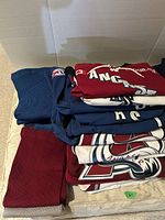 Stack of folded hockey jerseys and pairs of hockey socks, showing varied colors and logos including Ancaster hockey team.