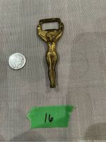 Front view of brass lady figure bottle opener next to a quarter for size comparison on a fabric background.