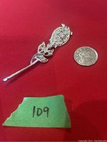 Full view of long stem rose brooch with rhinestones placed on red background next to a quarter for scale.