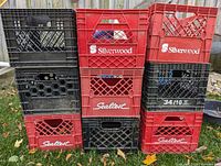 Photo of 9 plastic milk crates stacked and arranged outdoors on grass and leaves, showing red and black crates with Silverwood and Sealtest branding.