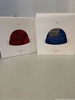 Two boxed Nike youth wireless headphone hats in red and blue colors as shown on front of packaging.