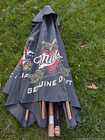 Folded Miller Genuine Draft patio umbrellas lying on grass, showing logo and wooden poles with crank handles