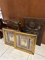 Wooden magazine rack with two framed pictures and a framed calligraphy painting next to it.
