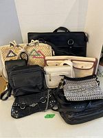 Photo showing a group of 9 assorted purses in varying styles including woven straw, black leather, and patterned fabric purses.
