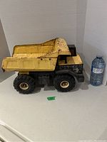 Side angled view of the Tonka dump truck next to a water bottle for scale, showing yellow bed, black cab, and wheels with signs of rust.