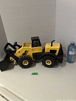 Side view of the Tonka front end loader toy showing the yellow loader arm and black bucket with large wheels, next to 1 liter water bottle for scale.