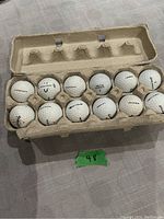 Photo showing 12 mixed used golf balls in a carton tray, brands include Callaway and TaylorMade, used condition with visible scuffs and dirt marks.