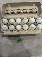 12 used golf balls arranged in a repurposed egg carton holder, majority Titleist brand, all white with visible wear and dirt marks.