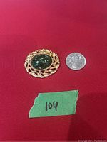 Front view of the vintage gold tone brooch with a large oval jade green stone, next to a coin for size reference.