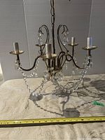 Front view of vintage metal chandelier with five arms, faux candle sockets, and hanging crystal bead garlands. Ruler in front shows width approx 18 inches.