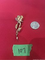 Front view of vintage long stem rose brooch placed next to a quarter for size reference against a red background.