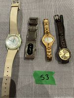 Four watches displayed on fabric surface with green tape label '53'