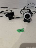 Photo of two wired webcams; one with circular LED ring light, one rectangular with dual lenses, both with USB cables.