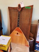 Front view of balalaika leaning against a cane-back chair, showing the full triangular body and neck.