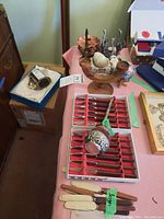 Photo showing various glass candle holders, carved stone egg, Buddha figure, Alpaca decor, and sets of side cutters in red trays on a table.