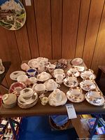 Overview of the table showing multiple tea cups, saucers, mugs, and plates set with floral and gold patterning.